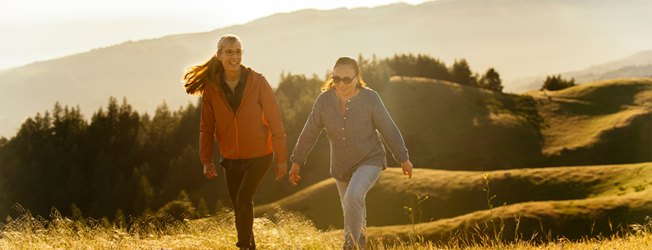 Image of two middle aged women taking a hike up a hill in the sunlight